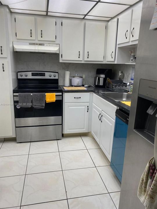Kitchen featuring white cabinetry with dark hardware, stainless steel appliances, dark countertops, a drop-in sink, and light-toned tile flooring