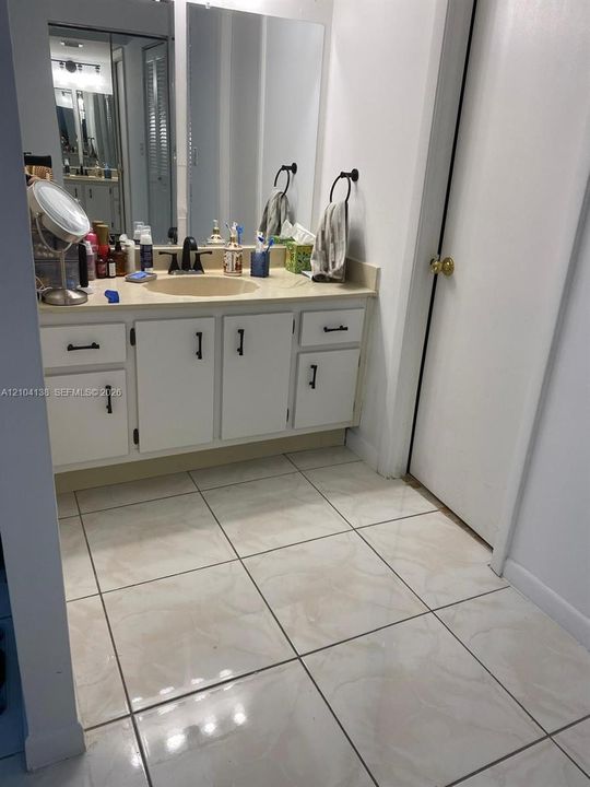 Bathroom vanity featuring white cabinetry, matte black hardware, a neutral countertop with an integrated basin, and a full-width wall mirror complemented by large-format ceramic floor tile