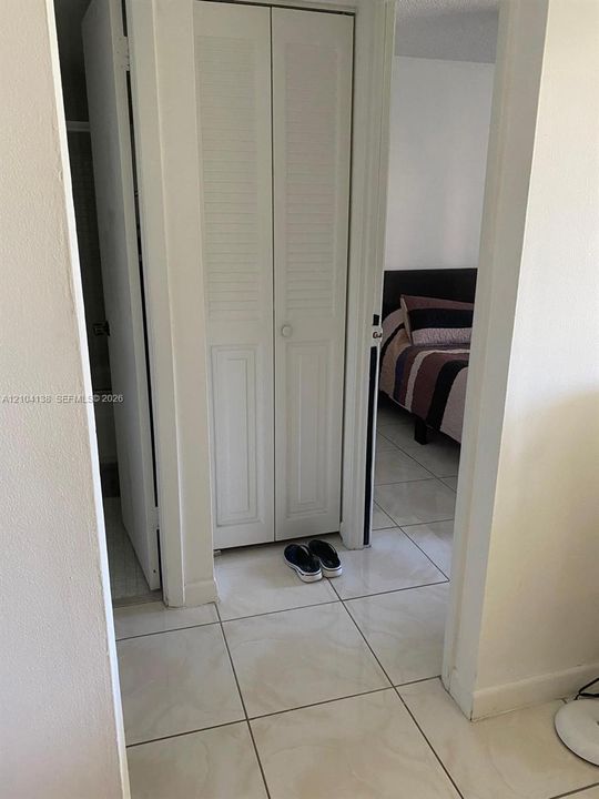 White bi-fold louvered closet doors, neutral-toned square tile flooring, and standard interior door hardware