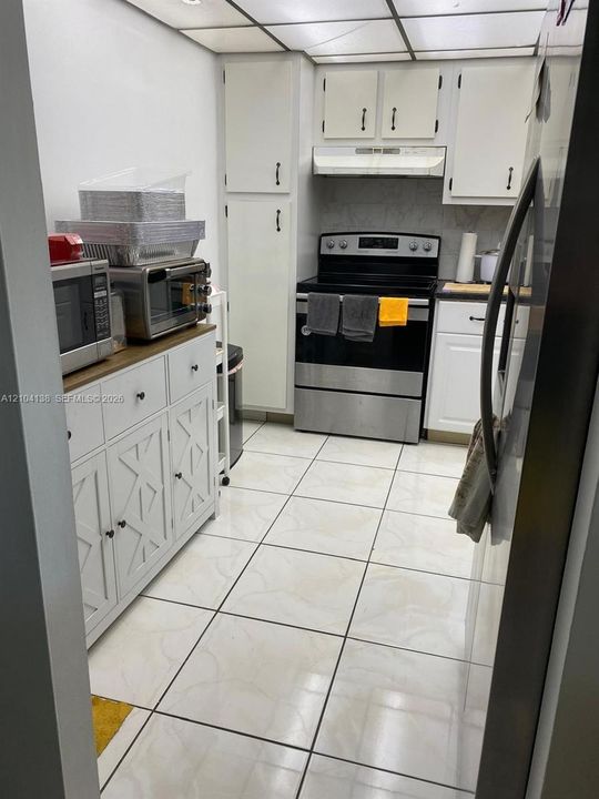 Kitchen featuring white shaker-style cabinetry, stainless steel range with overhead vent hood, and tiled flooring