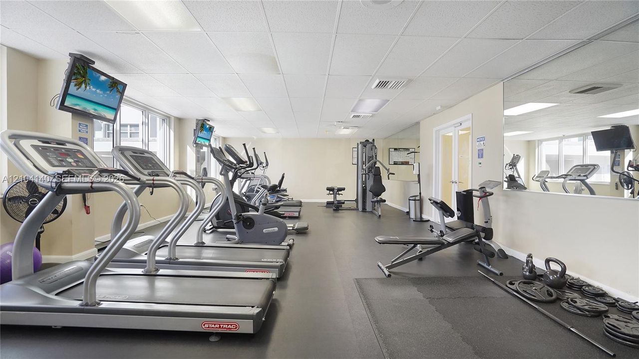 Fitness center featuring rubber flooring, wall-mounted mirrored panels, and drop ceiling with recessed lighting