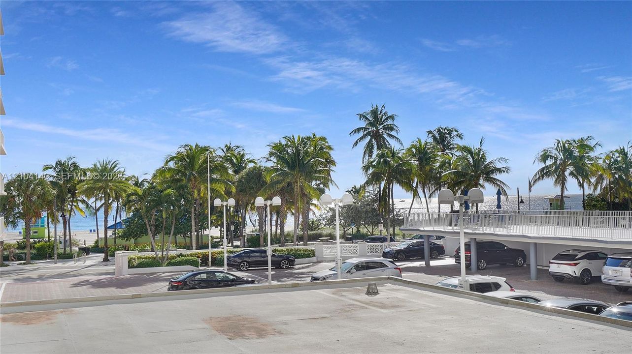 Outdoor terrace featuring a paved surface and white metal railing, overlooking a landscaped lot with mature palm trees and coastal scenery