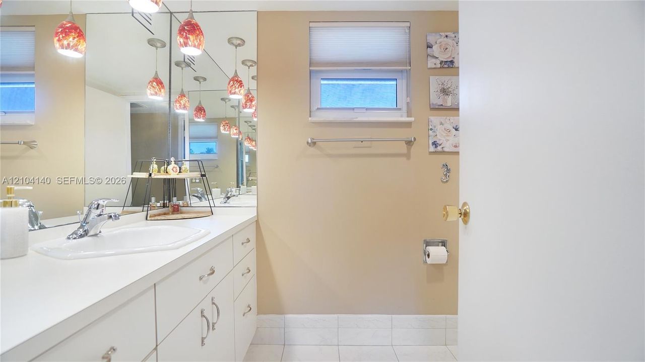 Bathroom featuring a white vanity with a composite countertop and integrated sink, large wall-mounted mirror, multiple pendant light fixtures, and ceramic tile flooring