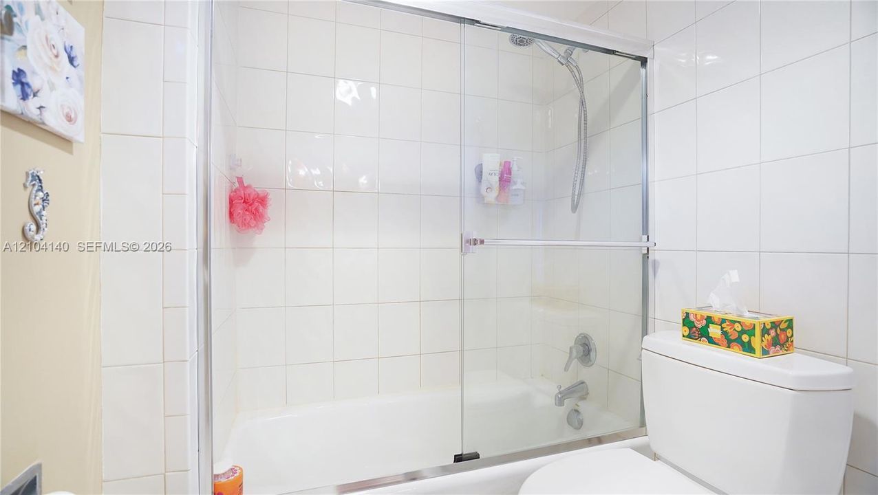Bathtub and shower combination featuring full-height white wall tiling, sliding glass enclosure, chrome fixtures, and a handheld shower head