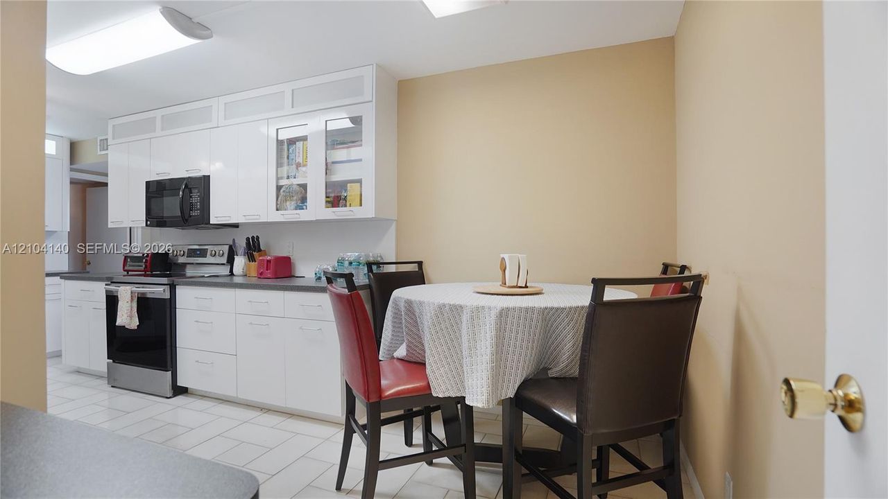 Kitchen featuring high-gloss white cabinetry, glass-paneled upper cabinets, stainless steel appliances, and ceramic tile flooring