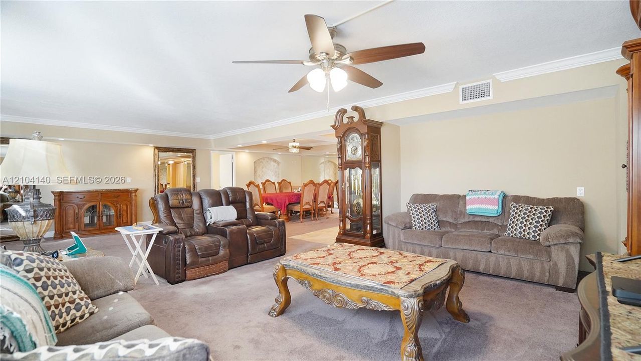 Spacious living area featuring crown molding, neutral wall color, carpeted flooring, and a ceiling-mounted light fixture with a fan