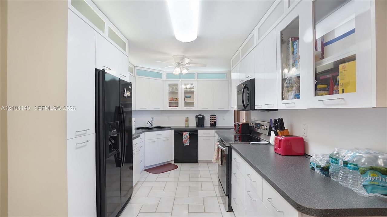 Kitchen featuring white cabinetry with glass-panel upper doors, dark stone-finish countertops, tile flooring, and integrated black appliances