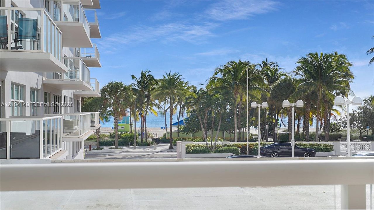 Private balcony featuring glass railings, overlooking palm trees and coastal scenery