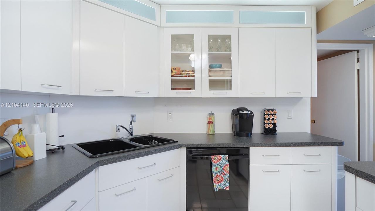 Kitchen featuring white cabinetry with glass-front display panels, transom accent windows, dark-toned countertops, and a dual-basin sink with a chrome faucet