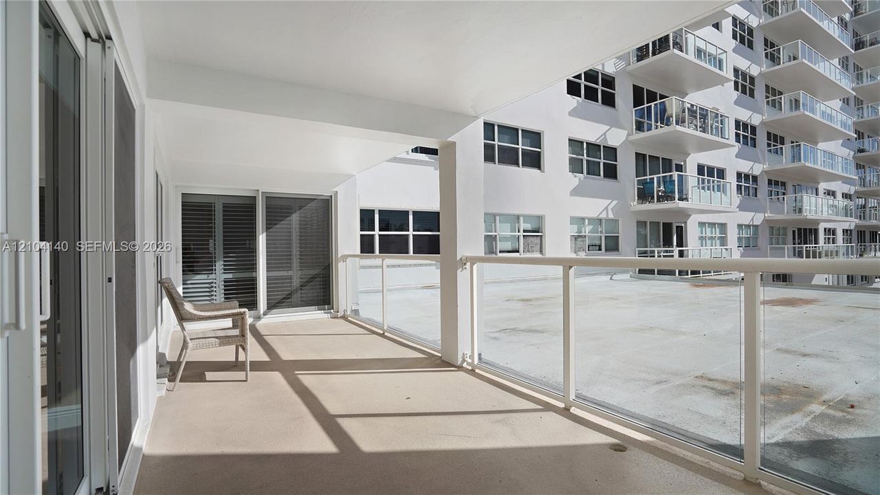 Covered balcony featuring glass pane railings, solid-surface flooring, and sliding glass door access