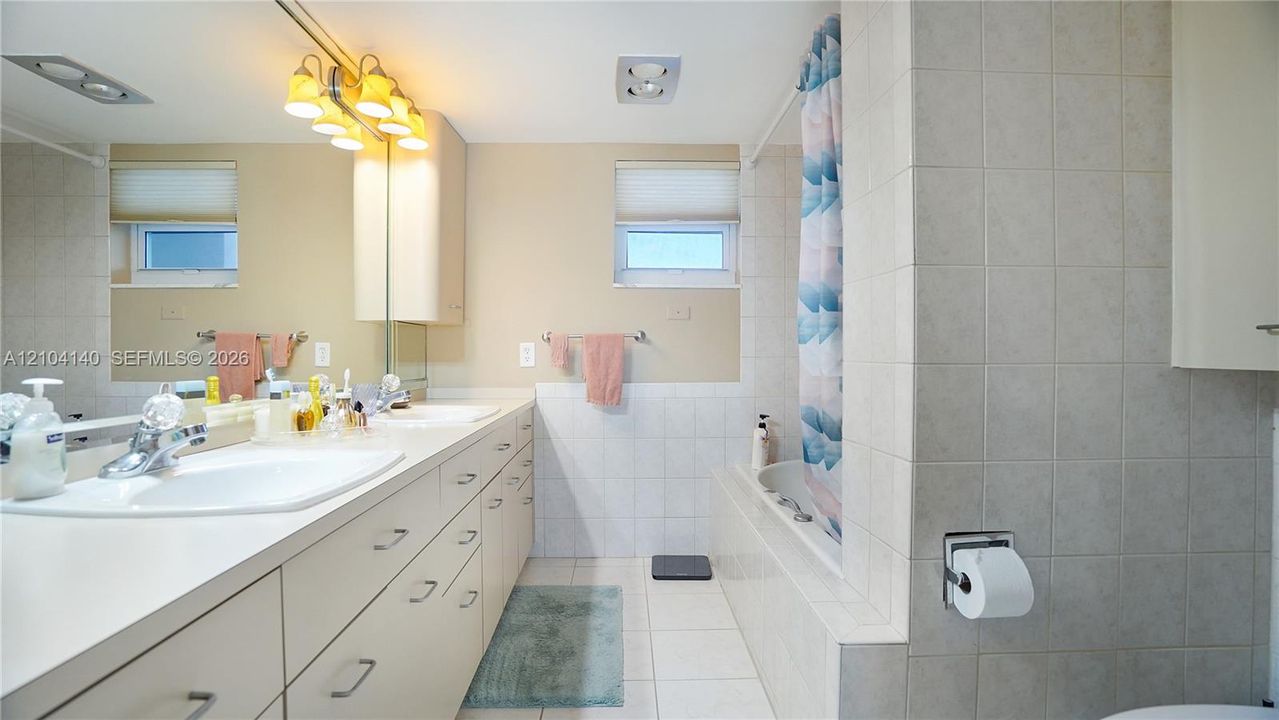 Full-width vanity with integrated dual sinks, expansive wall-to-wall mirror, built-in medicine cabinet, and a tiled bathtub surround