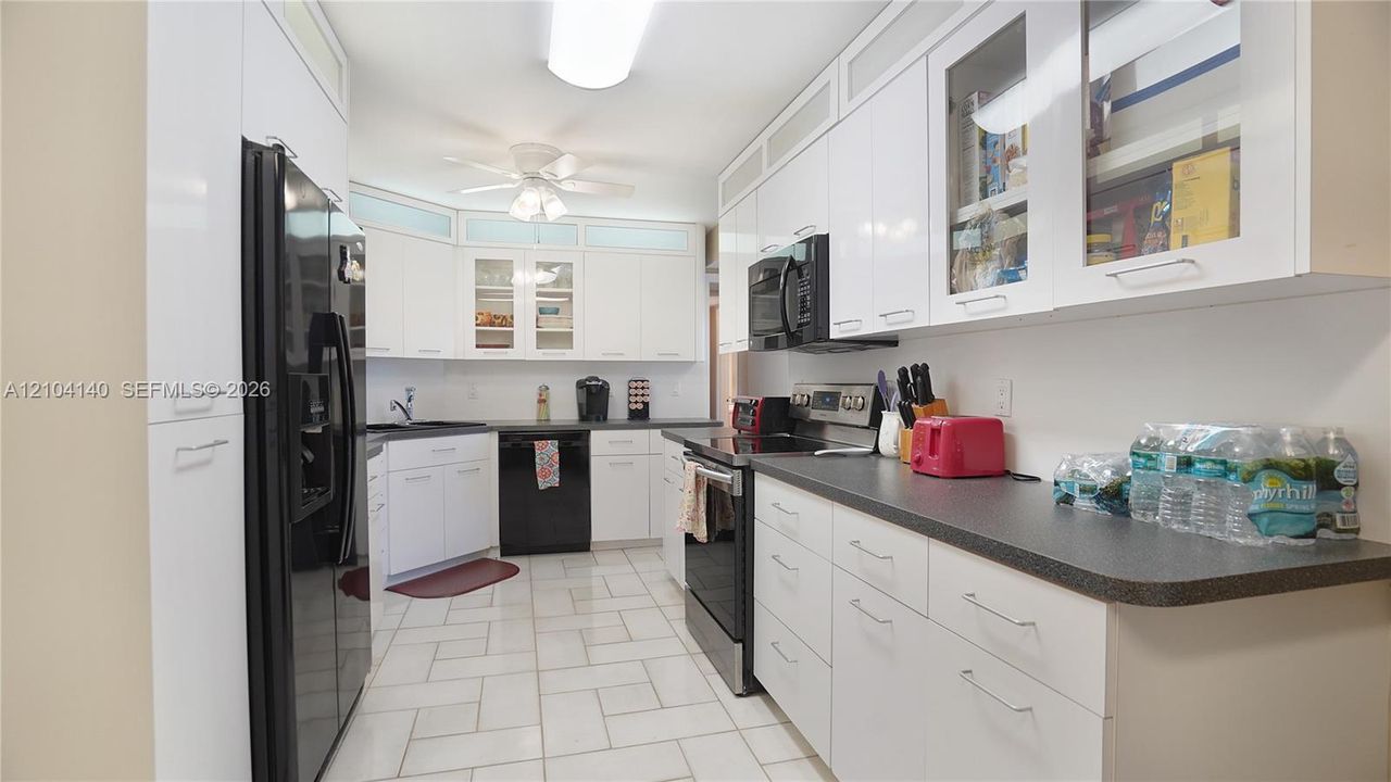 Kitchen featuring white cabinetry with glass-front uppers, solid surface countertops, tiled flooring, and integrated black appliances