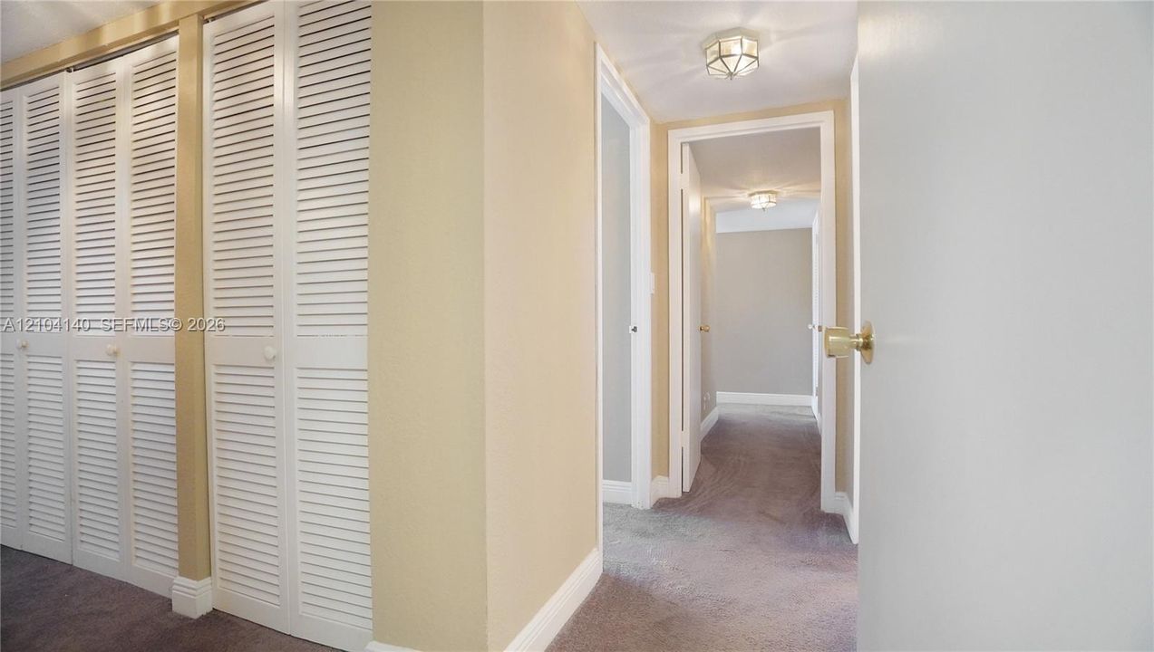 Hallway featuring wall-to-wall carpeting, floor-to-ceiling louvered closet doors, and flush-mount ceiling lighting fixtures