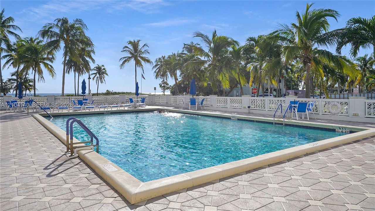 Swimming pool featuring a concrete deck, metal handrails, a geometric tile border, and a perimeter balustrade
