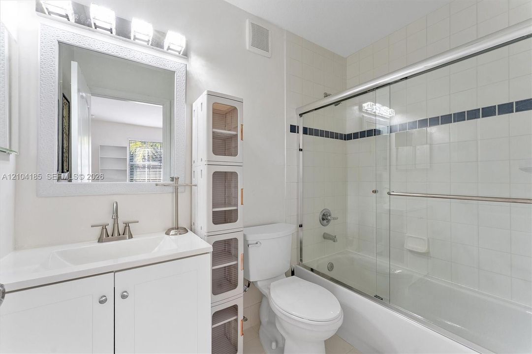 Bathroom featuring a white vanity cabinet with an integrated basin, a framed wall mirror, a multi-light fixture, and a combination shower and tub enclosure with sliding glass doors and tiled walls