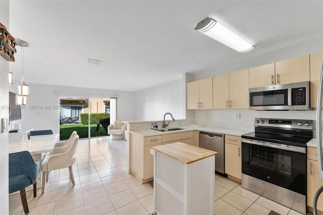 Kitchen featuring light-finish cabinetry, stainless steel appliances, ceramic tile flooring, and sliding glass doors leading to exterior space
