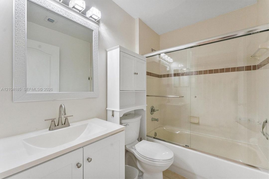 Bathroom featuring a vanity with an integrated sink, built-in over-the-toilet storage cabinet, framed wall mirror, and a tub-shower combination with sliding glass doors