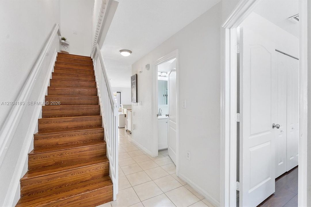 Staircase with wood-finish treads, white painted handrails, ceramic tile flooring, and multi-panel interior doors
