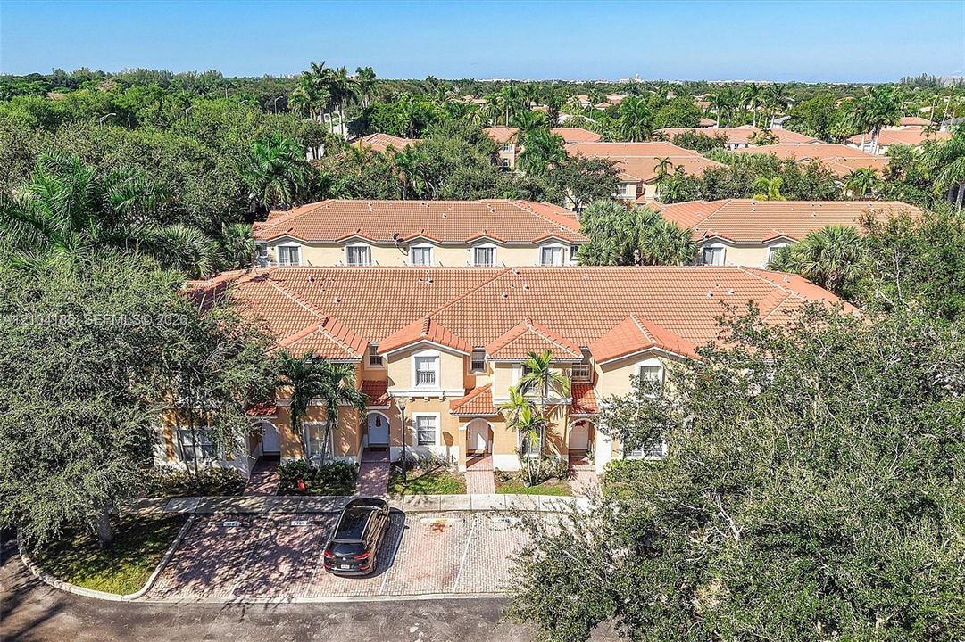 Two-story multi-unit structure with Mediterranean-style architecture, concrete tile roofing, paved parking areas, and mature landscaping