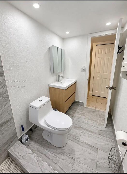 Bathroom featuring a wood-finish floating vanity, recessed ceiling lighting, a mirrored medicine cabinet, and large-format tile flooring