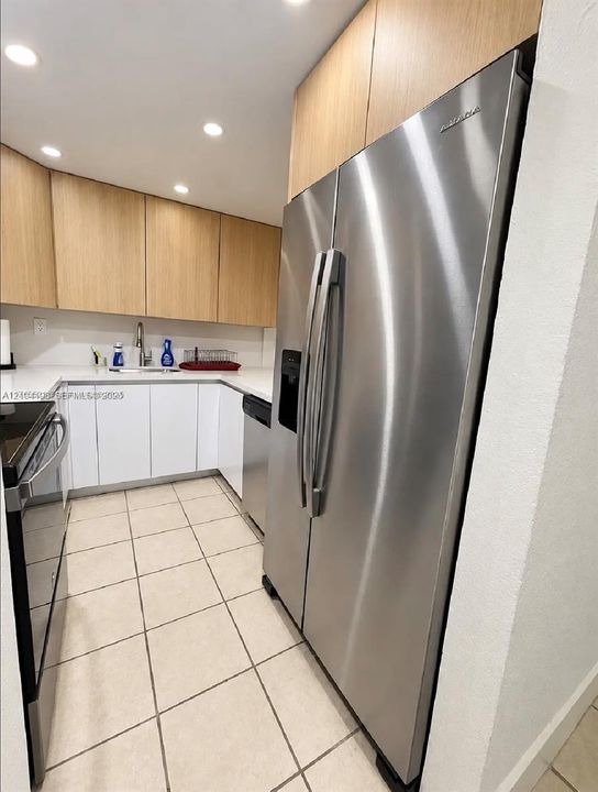 Kitchen featuring stainless steel appliances, white quartz countertops, light wood-finish cabinetry, and ceramic tile flooring