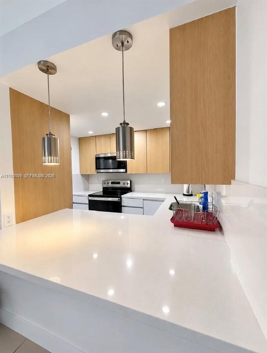 Kitchen featuring a quartz peninsula countertop, wood-finish cabinetry, stainless steel pendant lighting, and stainless steel appliances