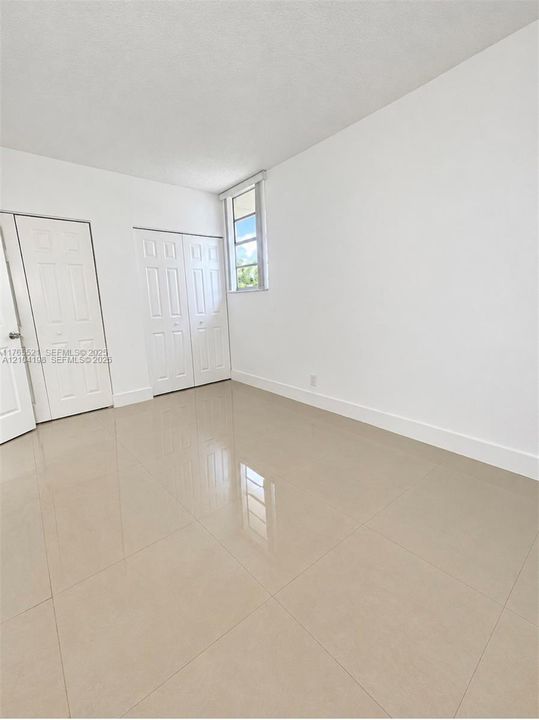 Interior space featuring neutral large-format tile flooring, white walls, two sets of white panel doors with brushed metal hardware, and a single vertical window