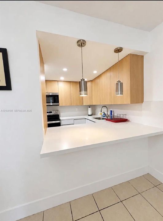 Kitchen featuring flat-panel wood-finish cabinetry, white solid-surface countertops, stainless steel appliances, and dual pendant lighting