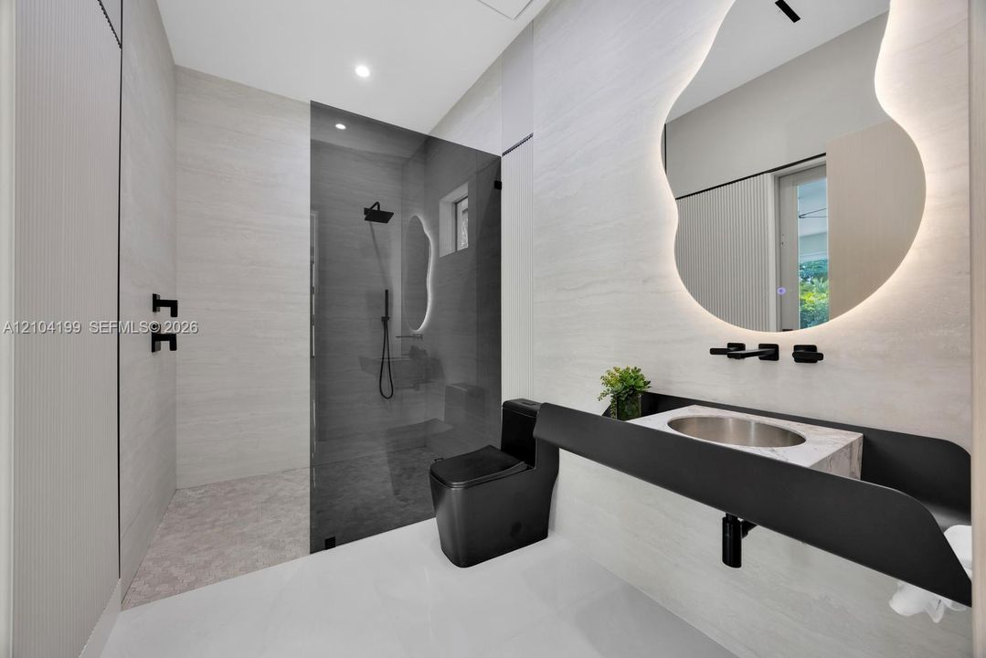 Bathroom featuring a wall-mounted floating vanity with a stone countertop, backlit organic-shaped mirror, matte black fixtures, and a walk-in shower with floor-to-ceiling tile
