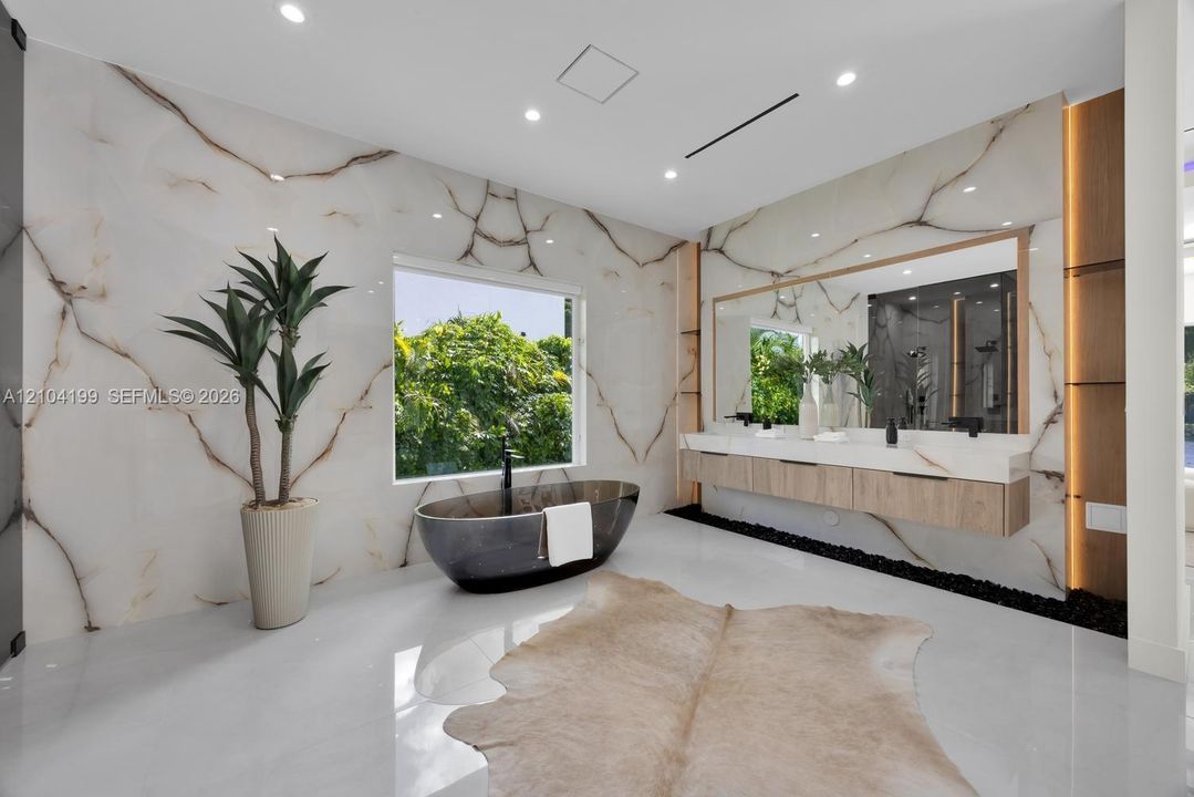 Full-height stone wall cladding with vein detailing, a freestanding dark basin soaking tub with wall-mounted plumbing, a dual-vanity floating cabinet with wood-finish cabinetry, a white countertop, and integrated LED accent lighting