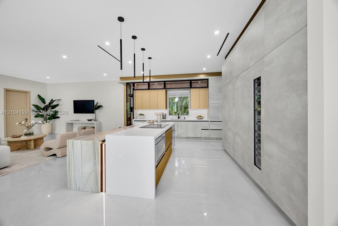 Kitchen featuring a central island with waterfall-edge countertop, floor-to-ceiling cabinetry with integrated beverage storage, matte metallic base accents, and linear pendant lighting