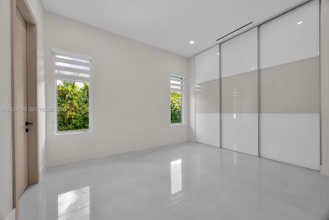 Polished tile flooring, floor-to-ceiling sliding glass-panel closet doors, and dual casement windows with integrated shades
