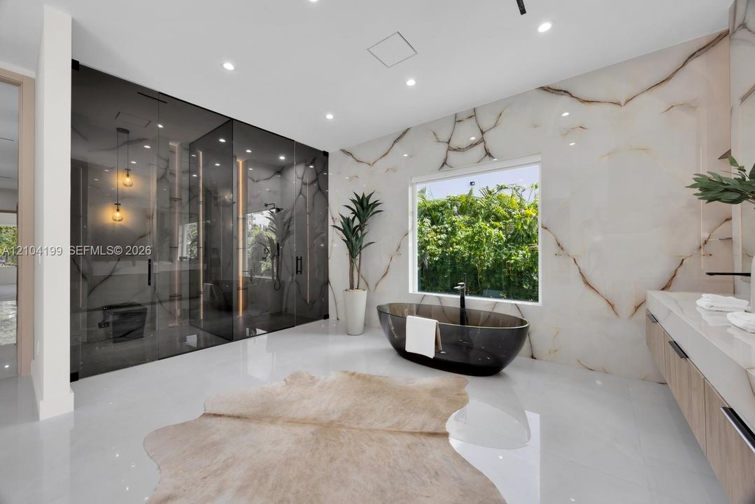 Bathroom featuring floor-to-ceiling stone wall cladding, a freestanding oval soaking tub, a smoked-glass enclosed shower, a floating vanity with stone surfacing, and polished large-format tile flooring