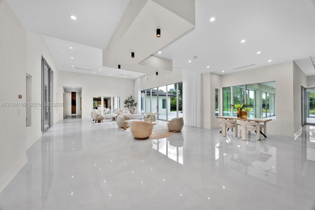 Open-concept living space featuring high-gloss tile flooring, recessed lighting, a tiered tray ceiling with cylindrical pendant fixtures, and floor-to-ceiling glass panel walls