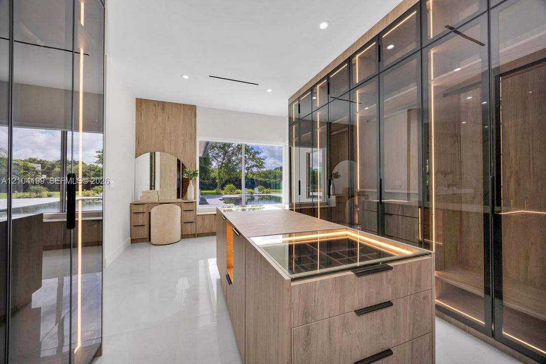 Custom built-in wood-finish cabinetry with full-height glass doors, integrated vertical LED accent lighting, central storage island with glass-top display, and built-in vanity station
