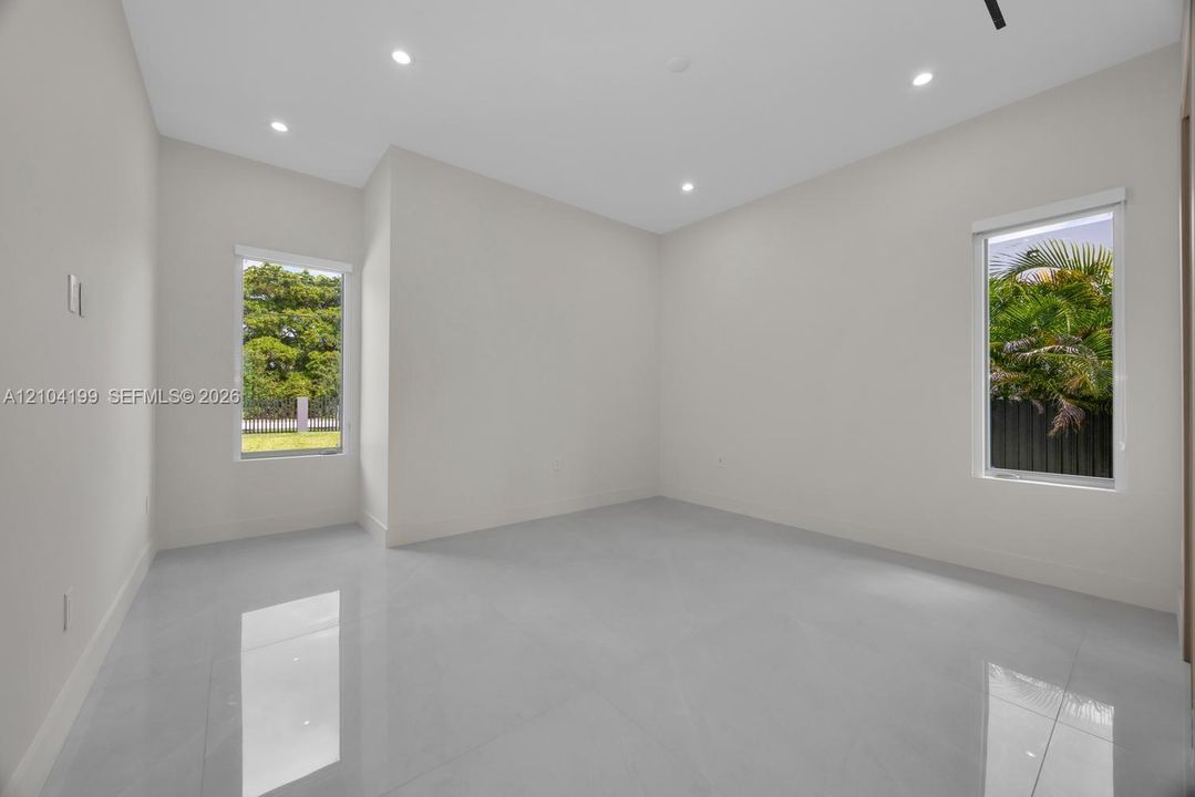 Neutral-toned interior room featuring large-format tile flooring, recessed ceiling lighting, and two windows providing natural illumination