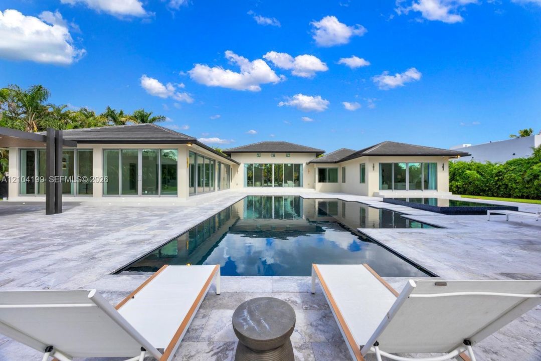 Outdoor living space featuring an expansive stone patio, a rectangular swimming pool, an attached spa, and floor-to-ceiling glass panel doors