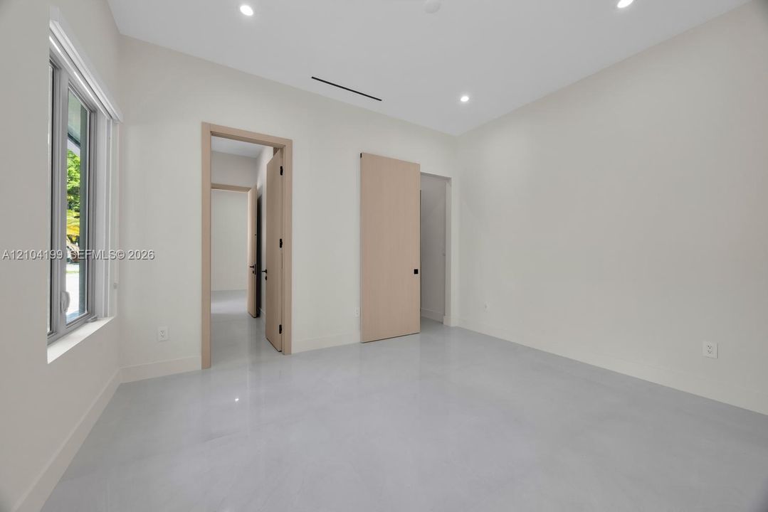 Neutral-toned room featuring smooth concrete-finish flooring, recessed lighting, light-wood interior doors, and a sliding barn-style door