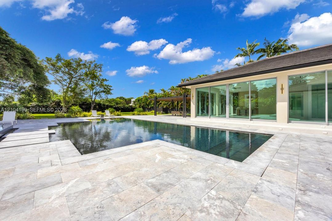 In-ground pool featuring a stone-tile deck, expansive glass sliding doors, and a covered patio area
