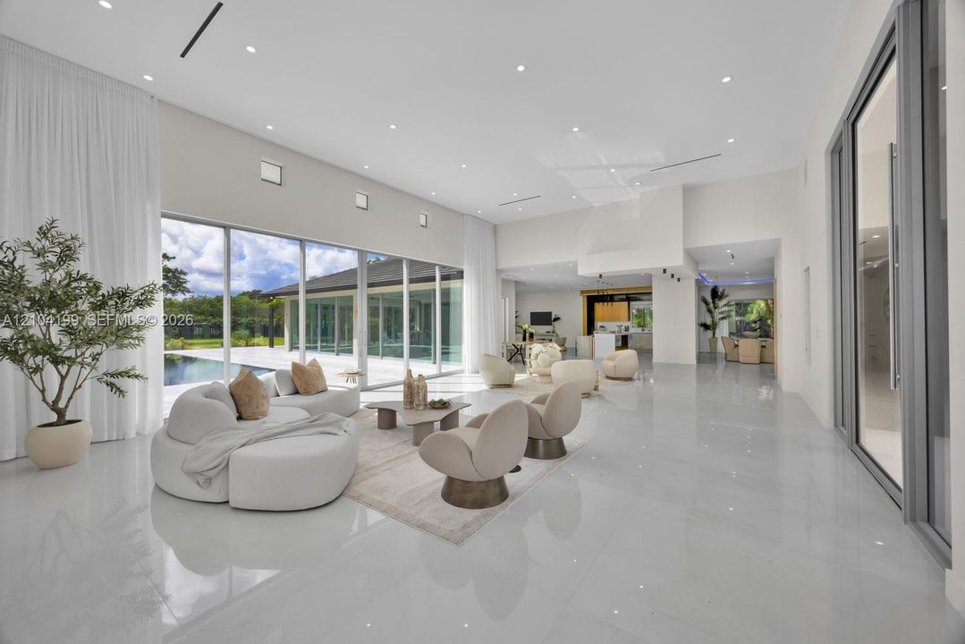 Expansive open-concept room featuring high ceilings with recessed lighting, large-format polished tile flooring, and floor-to-ceiling glass sliding doors