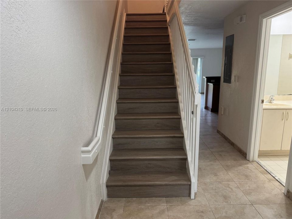 Staircase with wood-finish treads and white risers, featuring a white handrail and balusters