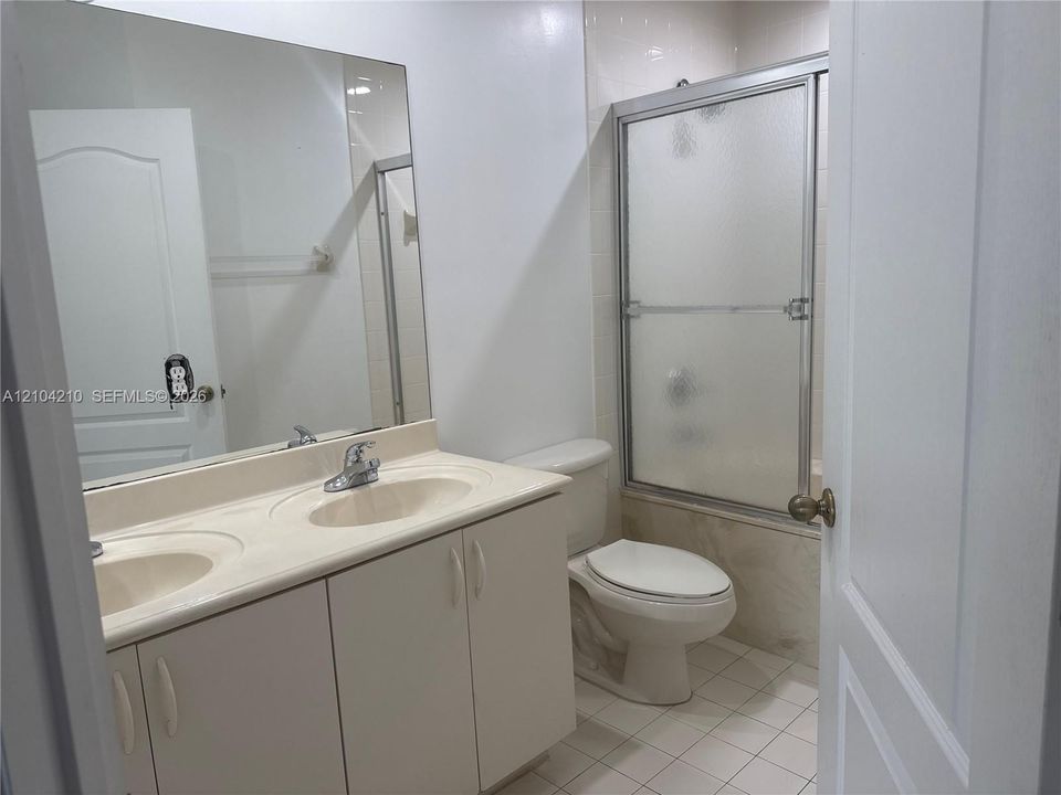 Double vanity with integrated sinks, large wall-mounted mirror, white tile flooring, and a shower-tub combination with frosted sliding doors