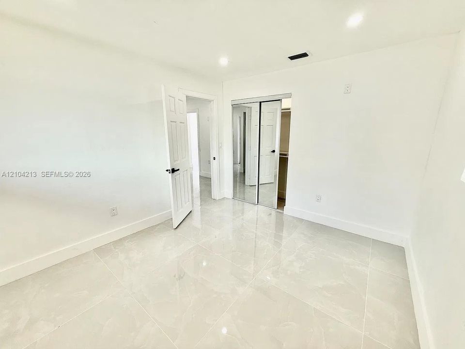 Spacious room featuring light-toned tile flooring, white walls, a recessed light fixture, and a mirrored closet