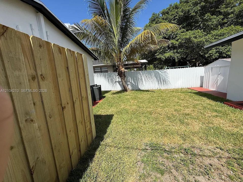 Fenced yard featuring a wooden privacy fence, a white perimeter fence, a mature palm tree, and a grass lawn