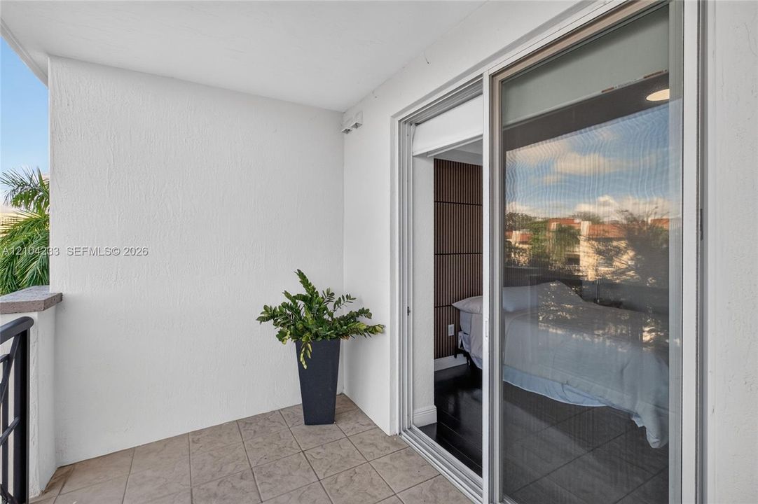 Private covered balcony featuring neutral floor tiling, textured stucco walls, and a metal railing
