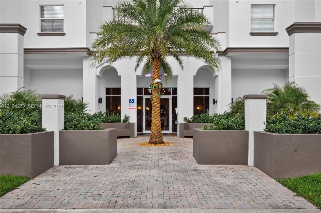 Exterior entryway featuring arched architectural detailing, paver stone walkway, and built-in masonry planters
