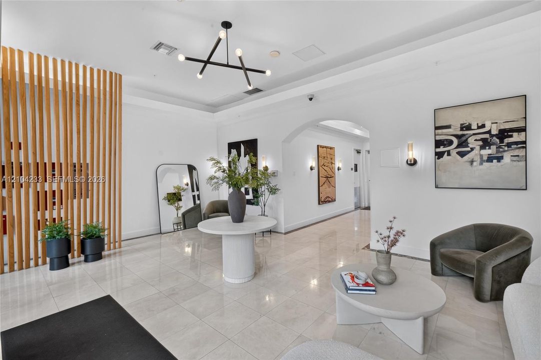 Lobby featuring floor-to-ceiling vertical wood slat screening, polished stone flooring, an arched entryway, and a geometric multi-arm chandelier