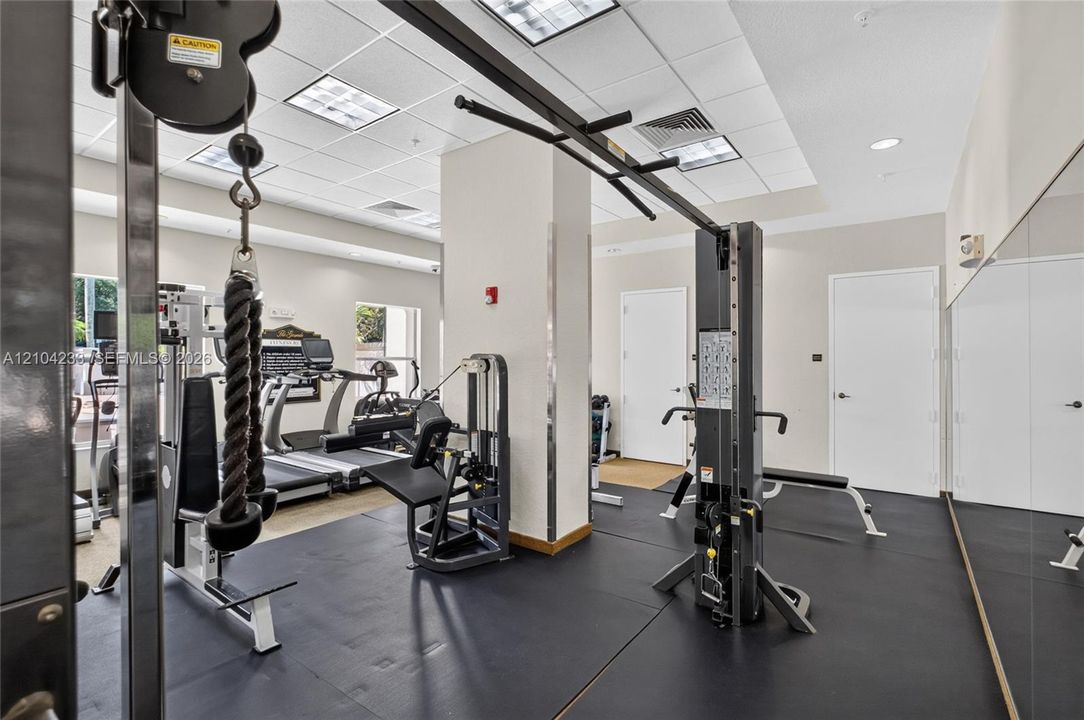 Fitness center featuring rubber flooring, recessed ceiling lighting, wall-to-wall mirrors, and neutral wall paint