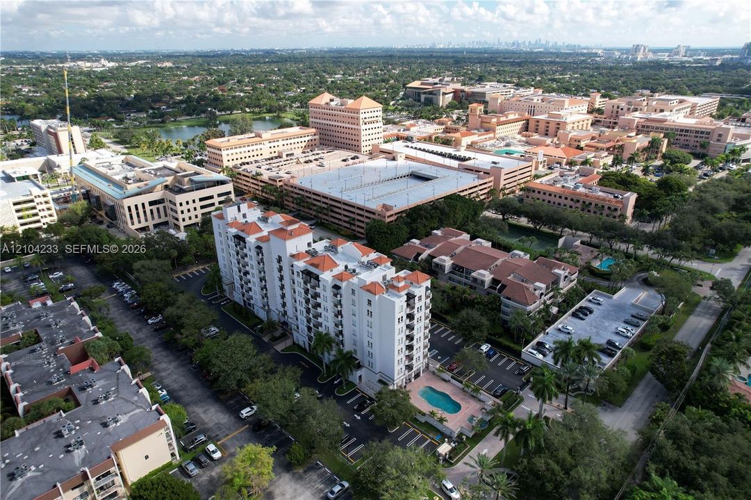 Multi-story residential building featuring a tile roof, dedicated surface parking, and a ground-level swimming pool with a paved deck
