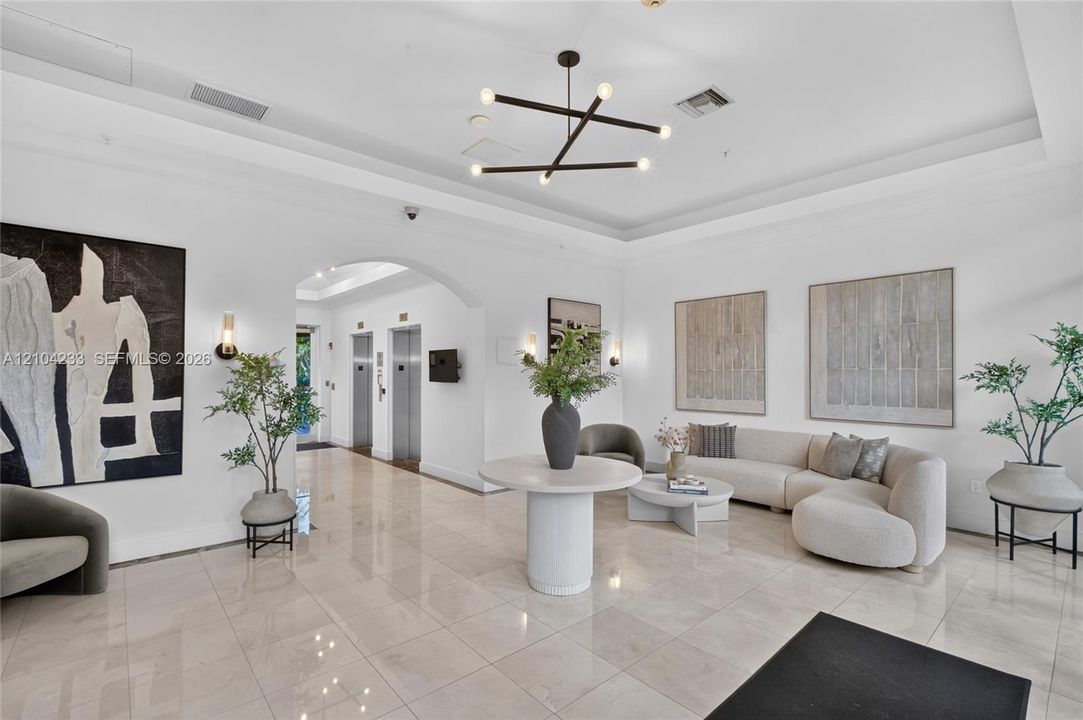 Lobby featuring high tray ceilings, polished tile flooring, metallic elevator doors, and a multi-arm modern pendant light fixture